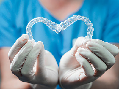 A person wearing white gloves holds a clear plastic heart-shaped object with transparent braces inside.