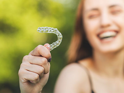 An individual holding a transparent dental retainer with a smile.