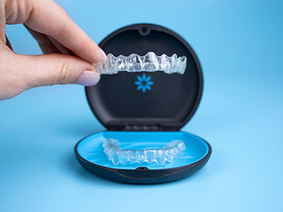 A person s hand holding an open blue dental impression tray with a clear plastic teeth mold inside it.