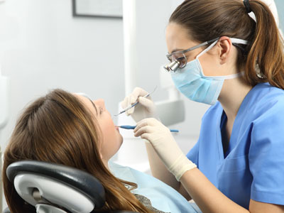 A dental hygienist is performing a cleaning procedure on a patient s teeth while wearing protective eyewear and gloves, with dental instruments visible.