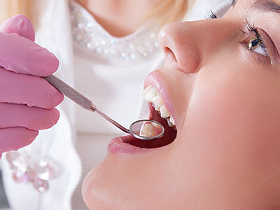 The image depicts a dental professional performing an oral examination on a patient s teeth using a dental mirror and a mouth prop, with a focus on the equipment being used for the procedure.
