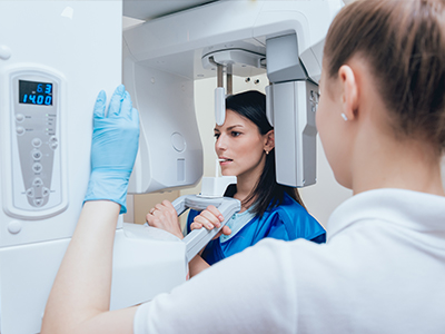 The image shows a woman in a blue lab coat standing next to a large, modern 3D scanner with a digital display screen, while another person appears to be inspecting the equipment.