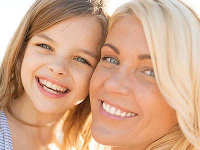 A woman and child are smiling at the camera against a beach backdrop.