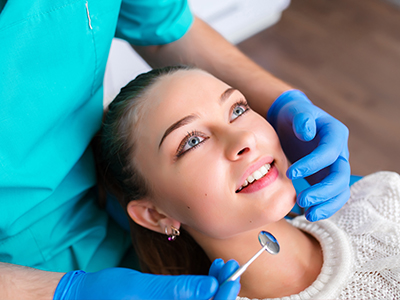 A person receiving dental care with a dental practitioner performing an examination, set against a clinical background.