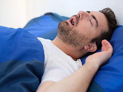 A man sleeping peacefully on a bed with blue sheets.