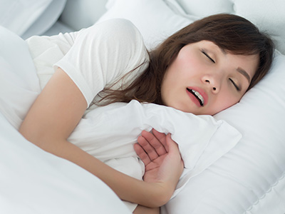 A woman is asleep on a bed with her hand over her mouth.